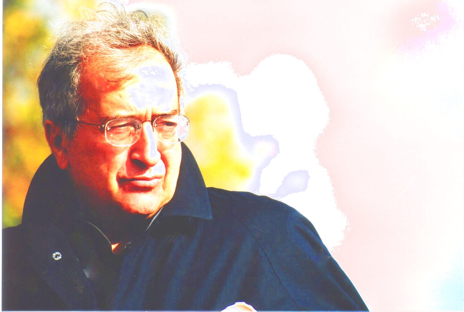 Zu sehen ist ein Portrait des Komponisten Luciano Berio. Im Hintergrund sind verschwommen Bäume und der blaue Himmel zu sehen. Er trägt einen dunklen Mantel und blickt zur Seite.