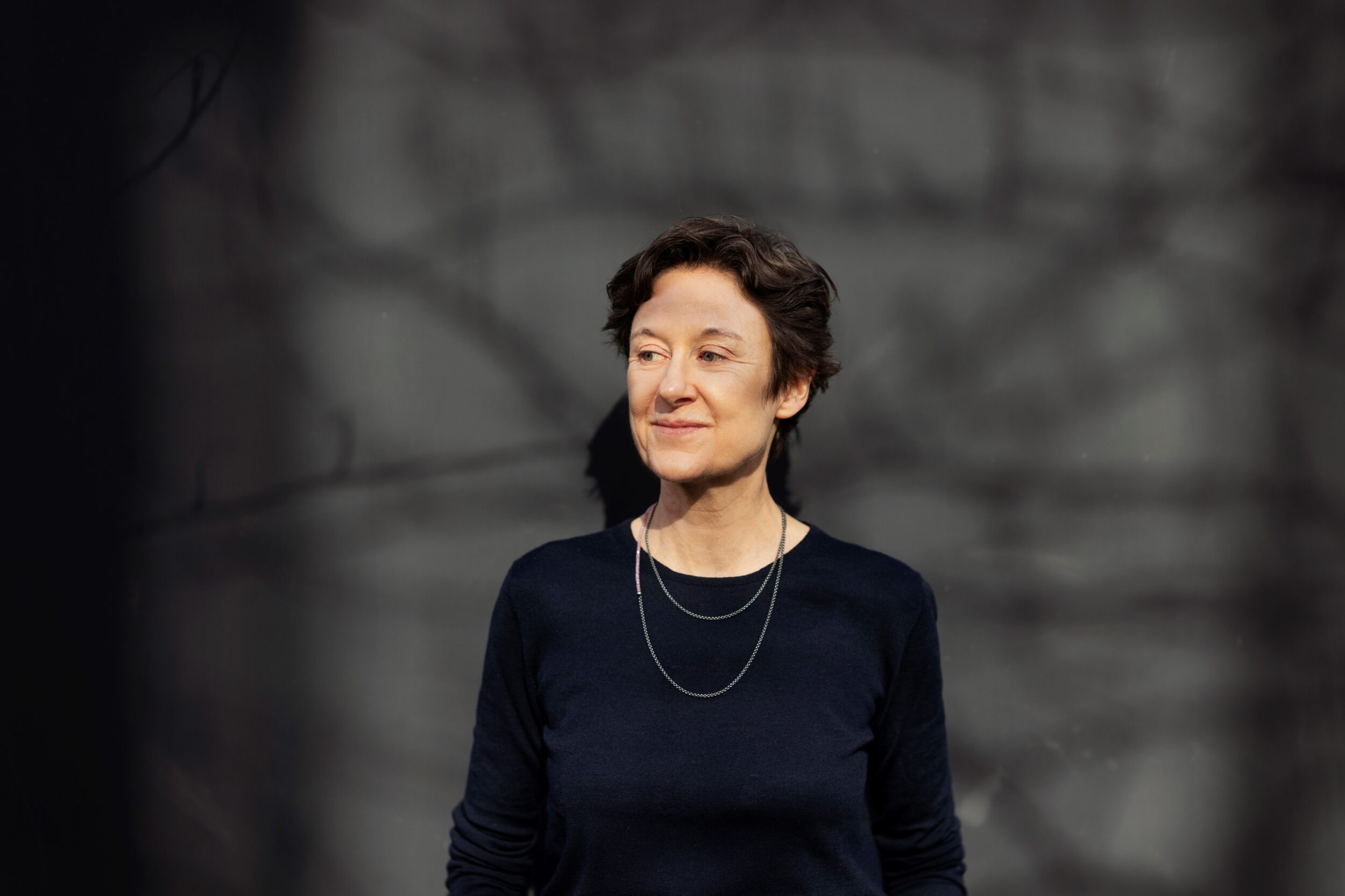 Zu sehen ist ein Portrait de Komponistin Isabel Mundry. Sie trägt ein dunkelblaues Oberteil und zwei silberne Ketten. Ihr Blick geht zur Seite.