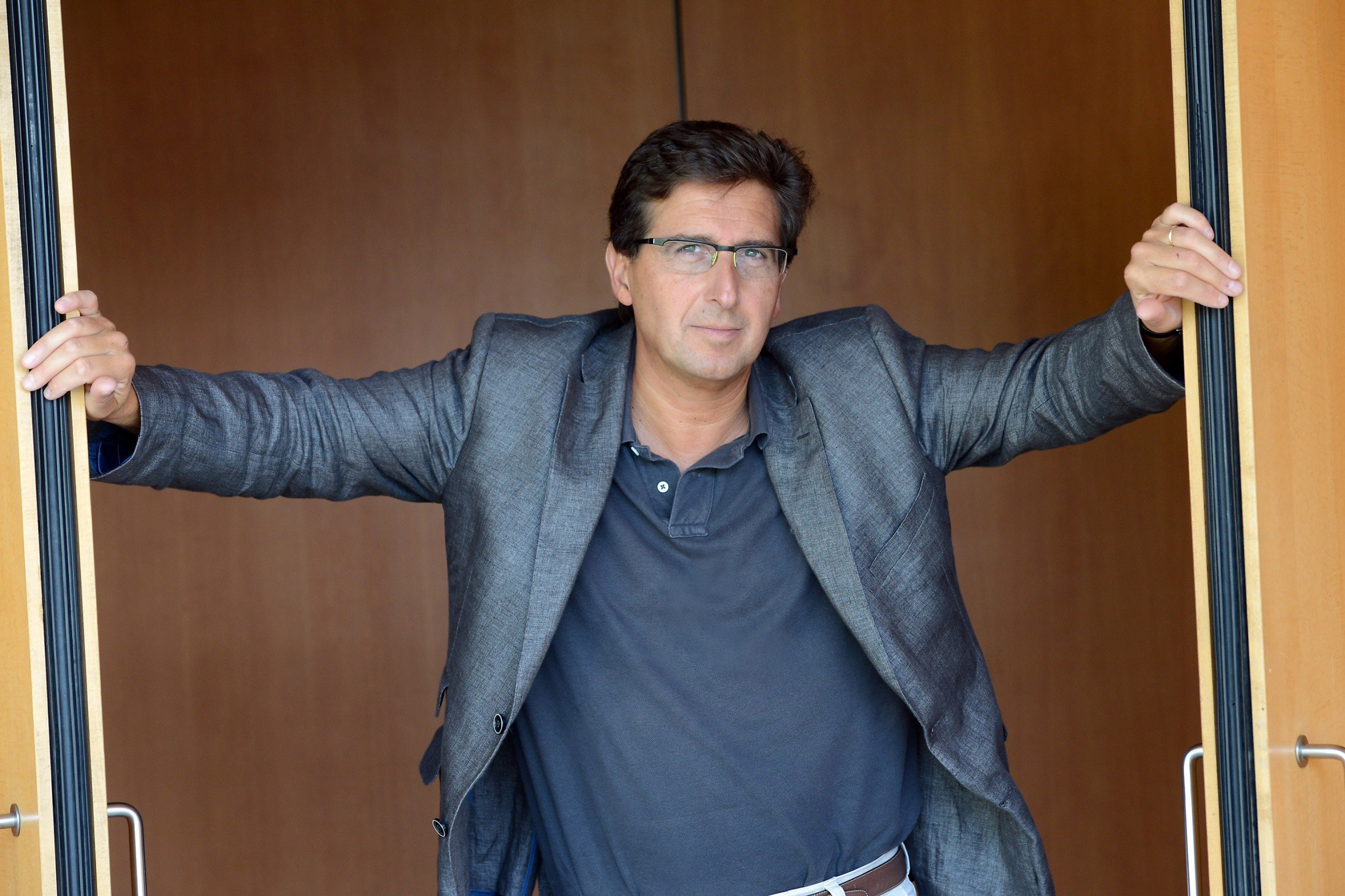 Zu sehen ist Pascal Rophé. Er steht in der Mitte einer Flügeltür und hält die zwei Flügel der Türe auf.